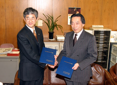 協定書を手に握手する岡田研究科長（右）と山本研究所長（左）
