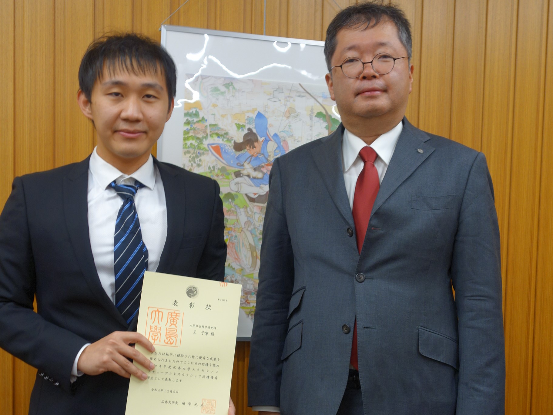 表彰状を持つ王さんと、永山プログラム長の記念撮影