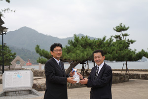 中村宮島観光協会会長（左）に消毒薬を手渡す二川教授