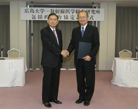 調印を済ませ握手する牟田学長（左）と佐々木理事長（右）。　場所は広島国際会議場の会議室