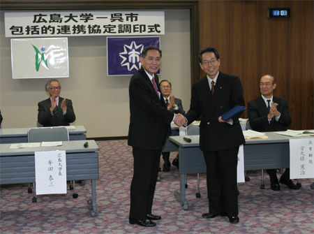 調印後，握手を交わす小村呉市長（右）と牟田学長（左）
