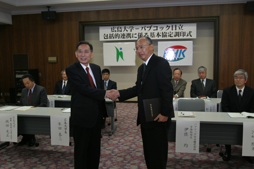 調印後，握手を交わす伊佐常務取締役（右）と牟田学長（左）
