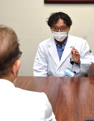安達病院長(手前)に報告する児玉助教