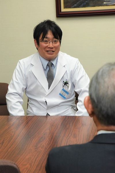 安達病院長(手前)に報告する松原助教