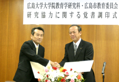 覚書に署名を済ませ握手する坂越正樹教育学研究科長（右）と岡本茂信教育長（左）