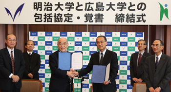 協定を交わし握手する明治大学・納谷廣美学長（左）と広島大学・浅原利正学長。締結会場は明治大学岸本辰雄記念ホール