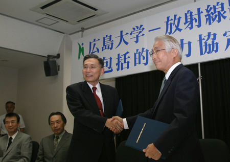 協定書に調印を済ませ握手する牟田学長（左）と大久保理事長