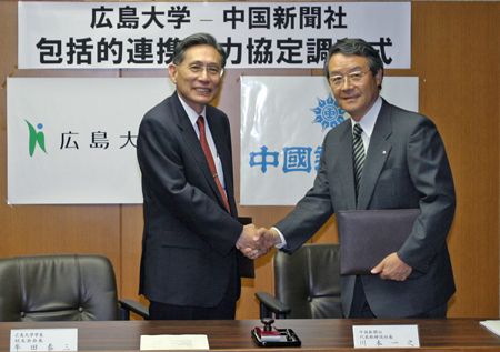 協定書に調印を済ませ握手する牟田学長（左）と川本中国新聞社代表取締役社長