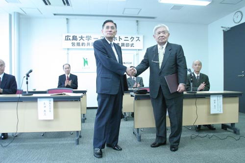 契約書に署名をすませ握手する牟田学長（左）と晝馬代表取締役社長（右）